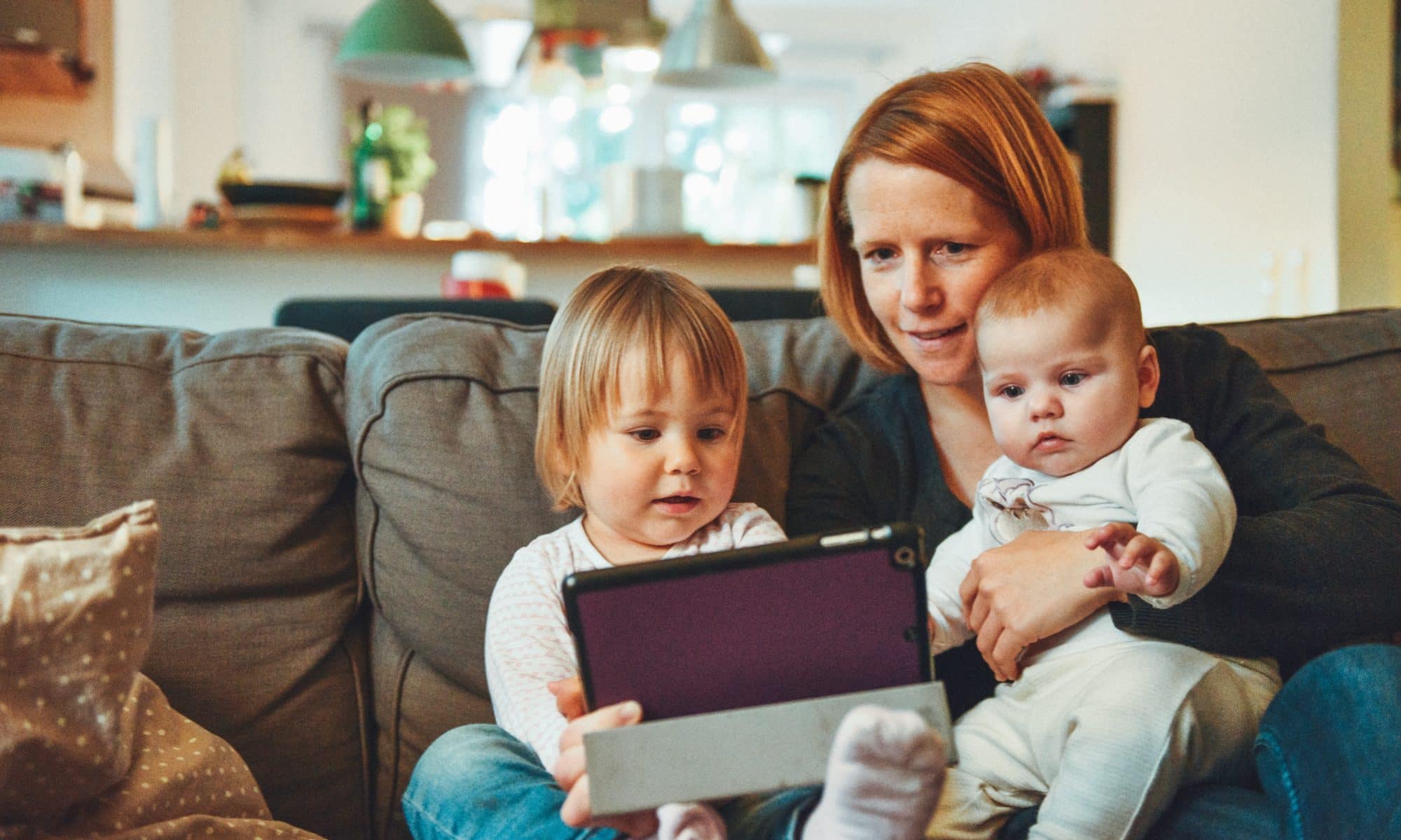 A woman and two babies playing with a tablet